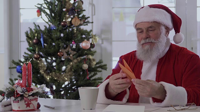 圣诞老人坐在圣诞树旁的桌子旁读祝福信视频下载