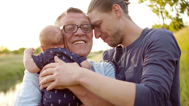 一个快乐的年轻人拥抱他的父亲和刚出生的儿子。父亲的爱。世代的延续。男性的温柔。父亲节视频下载