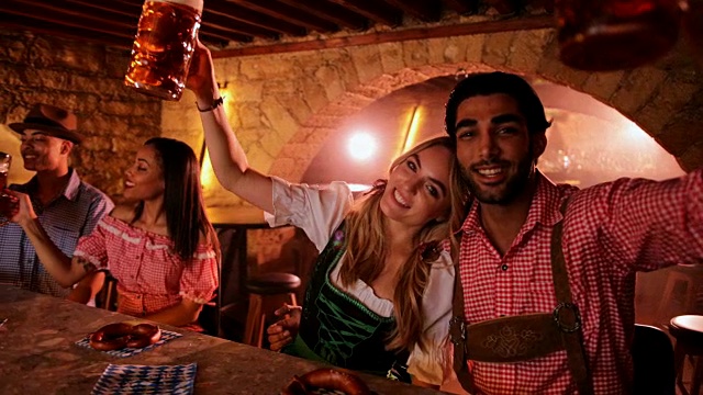 年轻夫妇在酒吧用啤酒和椒盐卷饼庆祝啤酒节视频素材