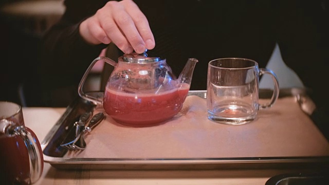 男子将一些蔓越莓茶从茶壶倒到杯子里。特写男人的手。视频素材