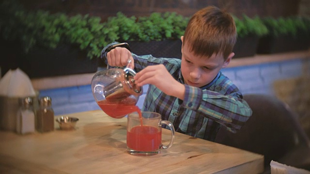男孩把一些蔓越莓茶从茶壶倒到杯子里视频下载