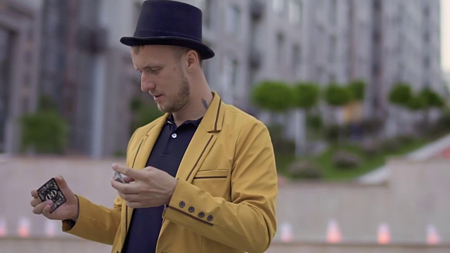 戴着帽子，穿着黄色夹克的魔术师熟练地在手里移动扑克牌视频下载