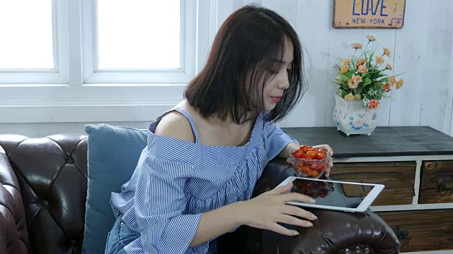 年轻女子在沙发上用笔记本电脑，吃着西红柿视频素材