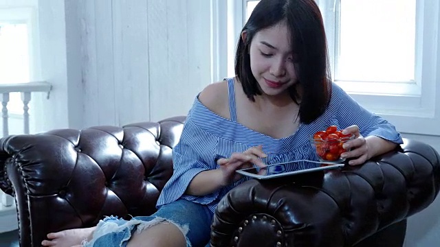 年轻女子在沙发上用笔记本电脑，吃着西红柿视频下载