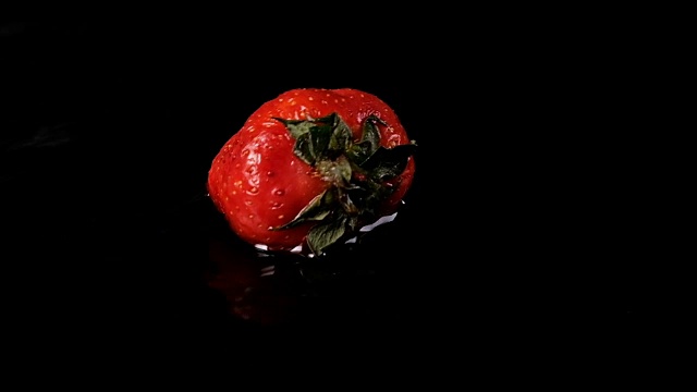 一个草莓掉进水里，背景是黑色的。慢动作视频下载
