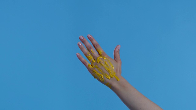 一个时尚模特的手在蓝色背景上画黄色的特写。时尚视频。视频下载