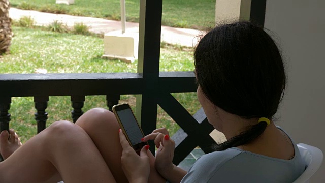 深色头发的女人在户外阳台上用手机在社交网络上聊天视频下载