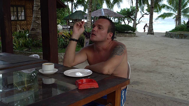 一个男人坐在街上的一张桌子旁，喝着咖啡，抽着烟视频素材