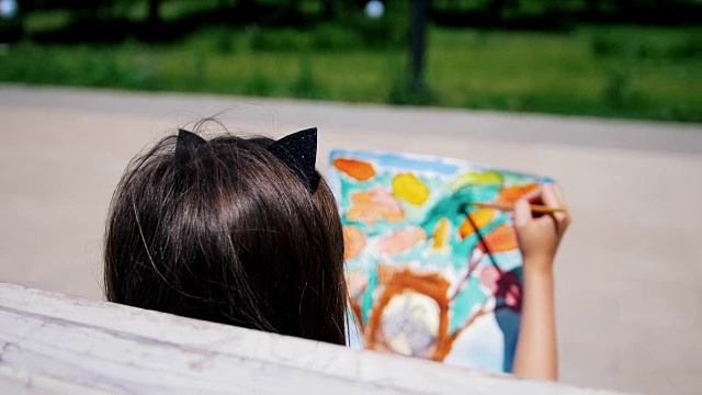 坐在公园长椅上画水彩画的小女孩的后视图视频下载