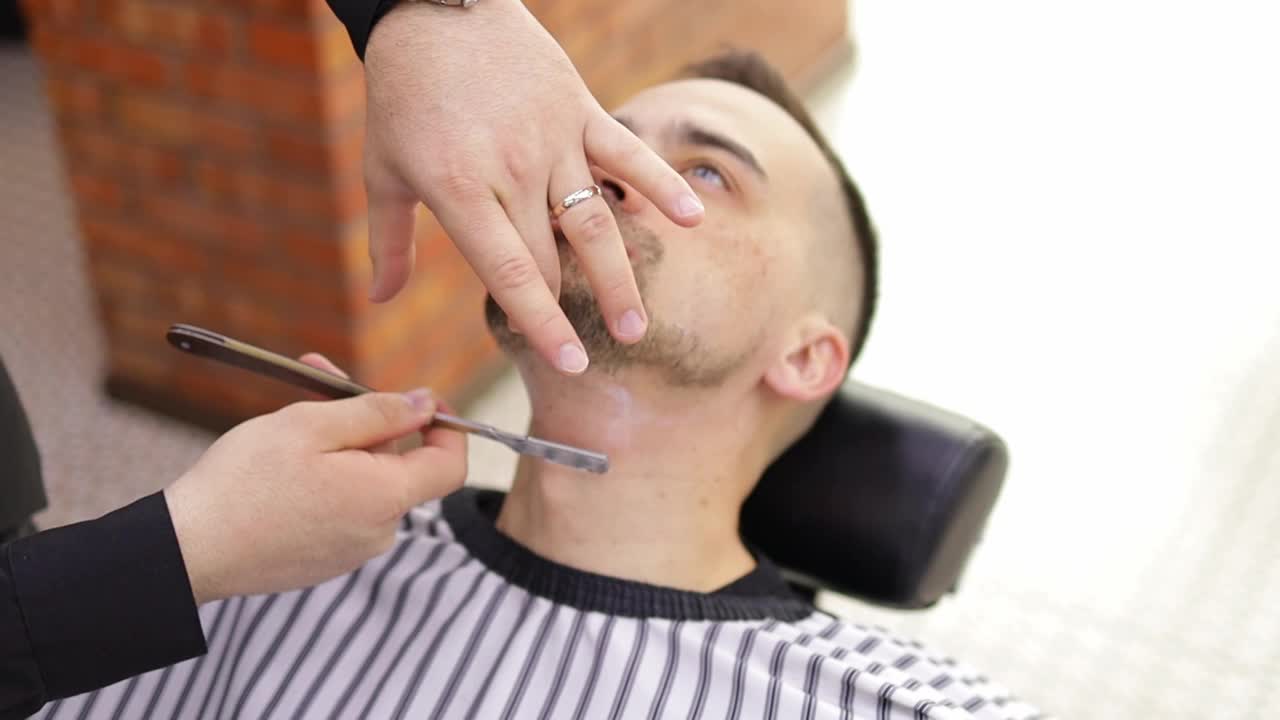 理发店里,理发师正在用一把老式直刀给顾客刮胡子