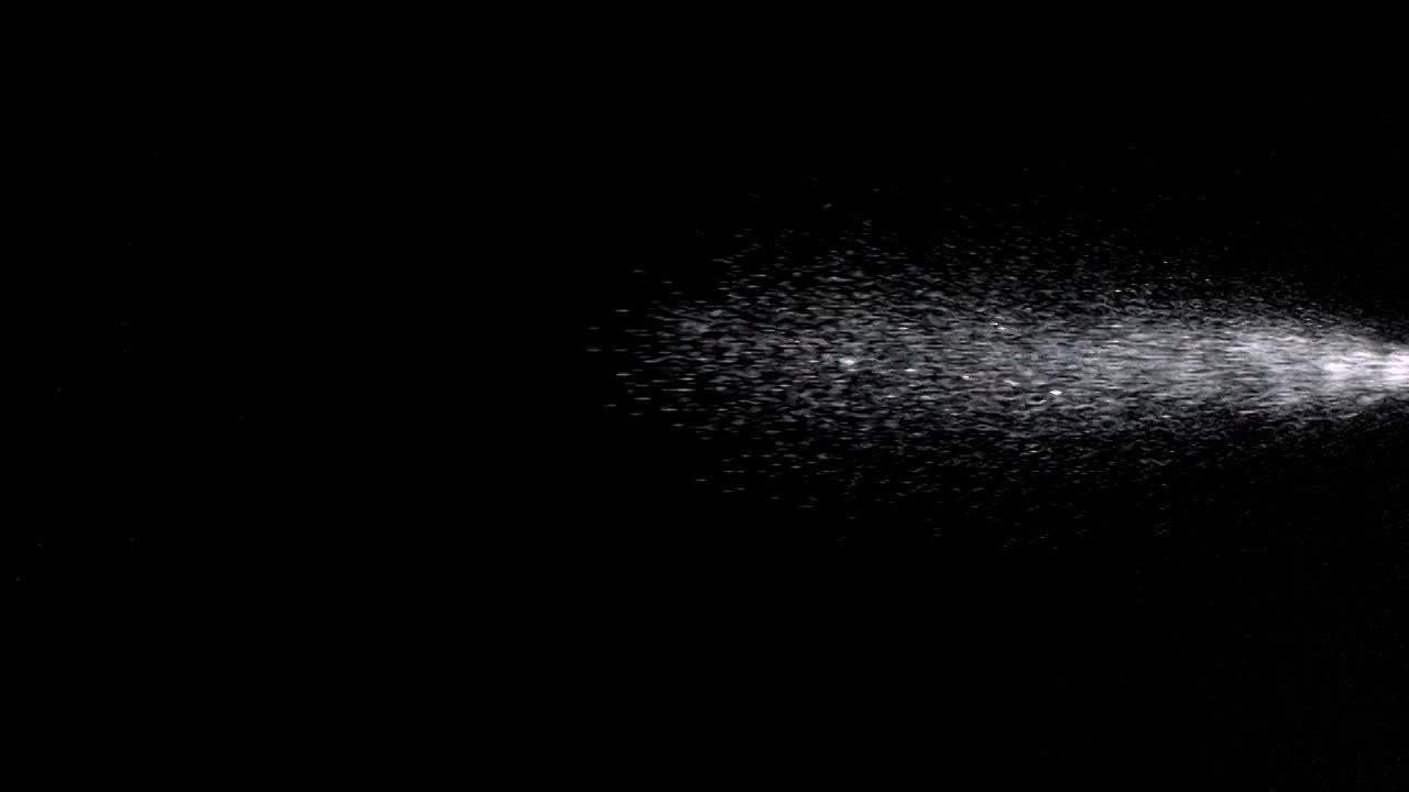 在一个黑色背景上，从喷雾器瓶中喷射的水滴进入并穿过画面的超慢运动视频素材