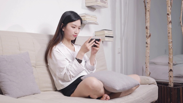 坐在沙发上的美女，使用手机打游戏视频素材