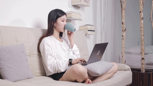 坐在沙发上的美女，边用电脑边喝咖啡视频素材
