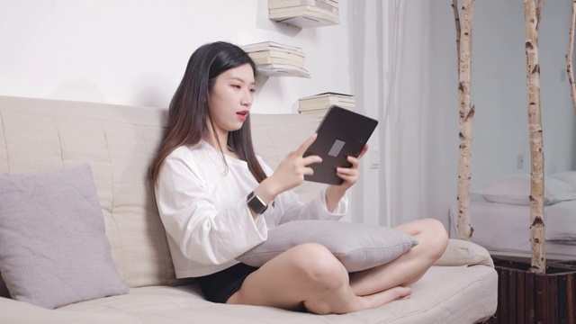 坐在沙发上的美女，正在用平板电脑玩游戏视频素材