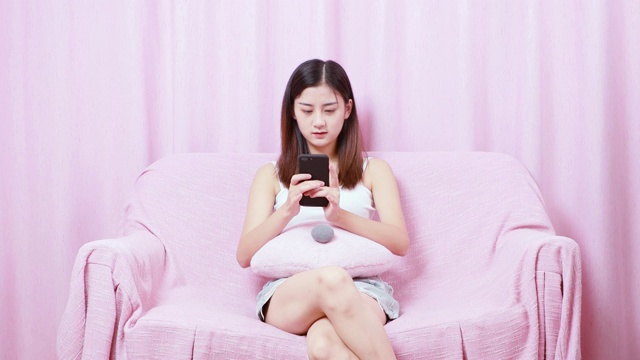 可爱的中国女孩，坐在沙发上正在用手机打字视频素材