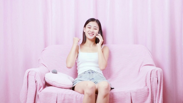 可爱的中国女孩，坐在沙发上正在打电话，然后感到很高兴视频素材