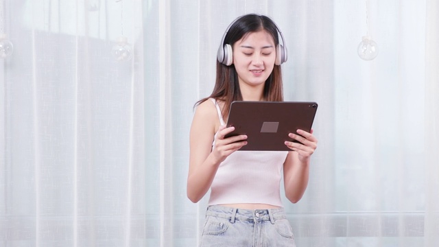 可爱的中国女孩，带着耳机看着平板电脑念英语视频素材