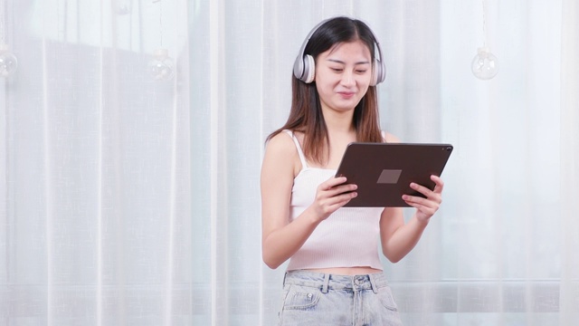 可爱的中国女孩，带着耳机看着平板电脑视频素材