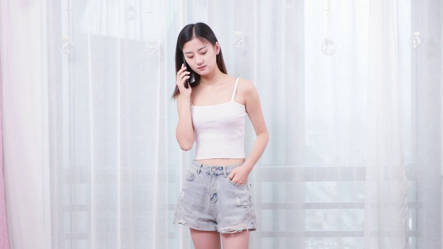 可爱的中国女孩，正在家里站着打电话视频素材