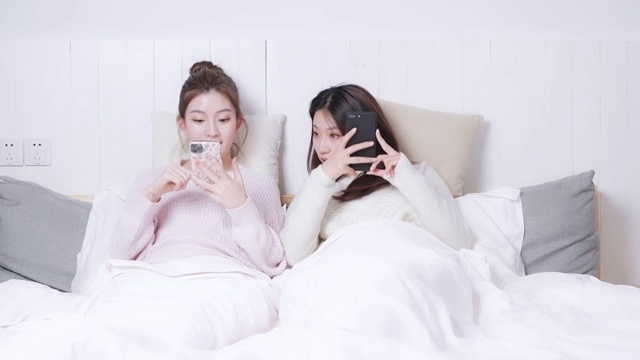 躺在床头正在玩手机的两位美女视频素材