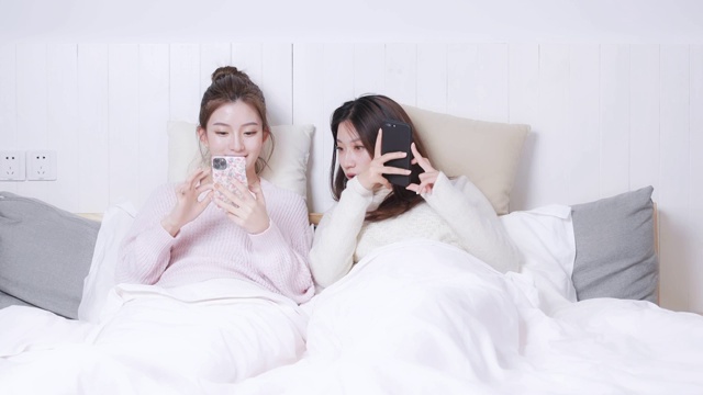 躺在床头正在玩手机的两位美女视频素材