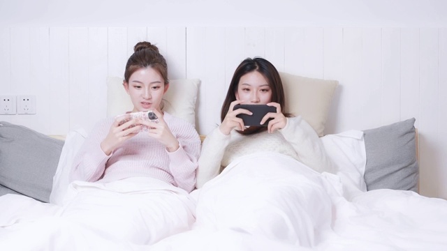 躺在床头正在玩手游的两位美女视频素材