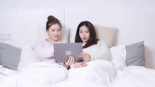 躺在床头正在使用平板电脑的两位美女视频素材