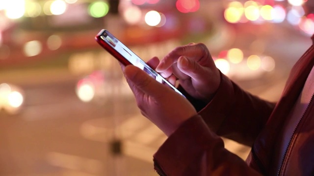 一个女人晚上在城市街道户外使用手机特写视频素材