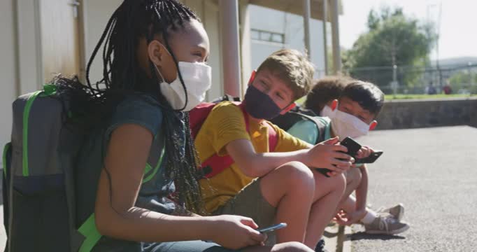 一群孩子戴着口罩坐在一起玩智能手机视频下载