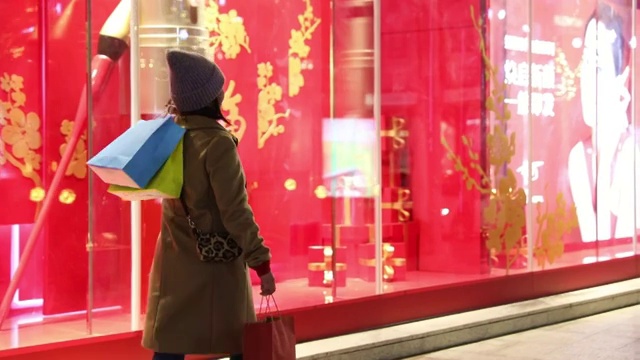 冬天夜晚拿着购物袋走在城市户外街道上的女人背影，春节购物概念视频素材