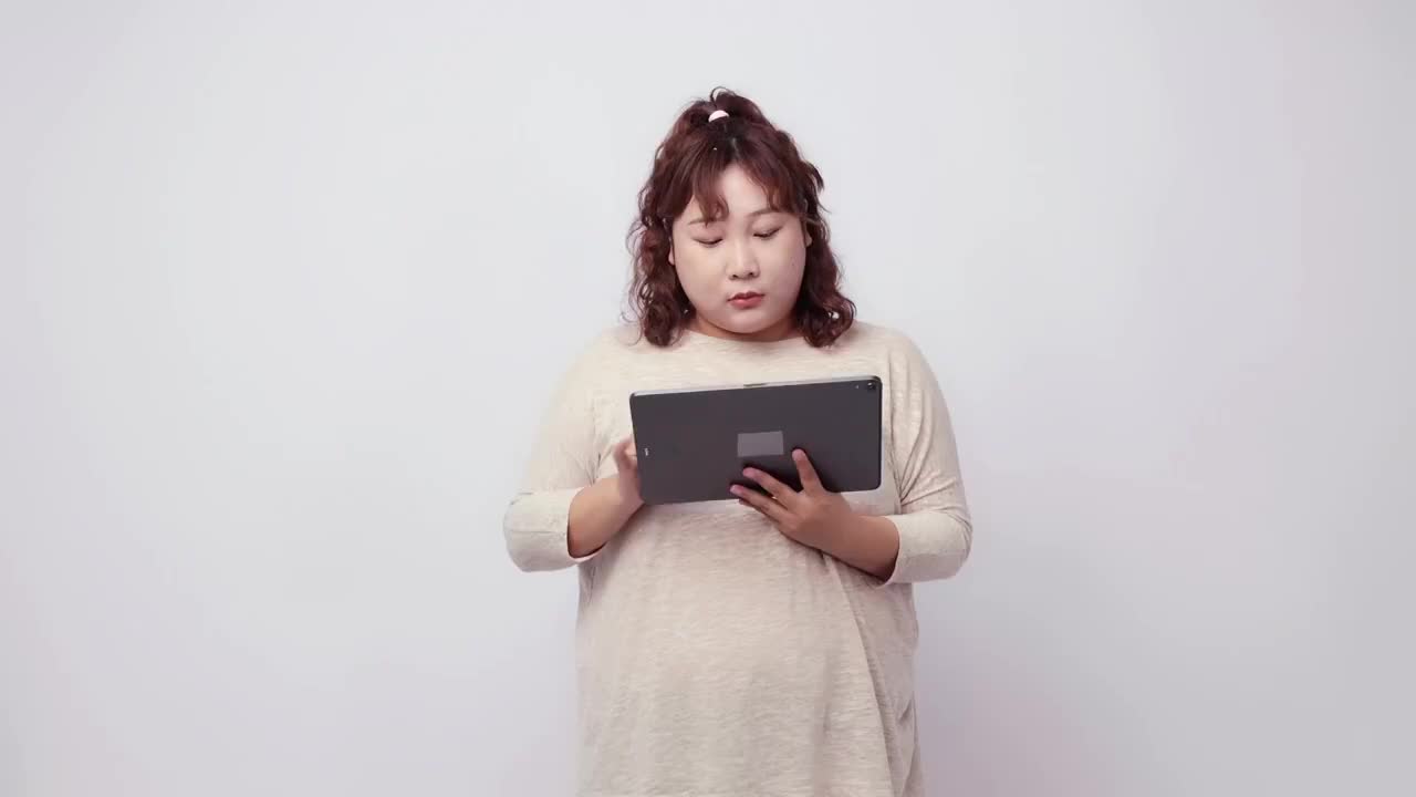 纯色背景里使用平板电脑的胖女孩视频素材