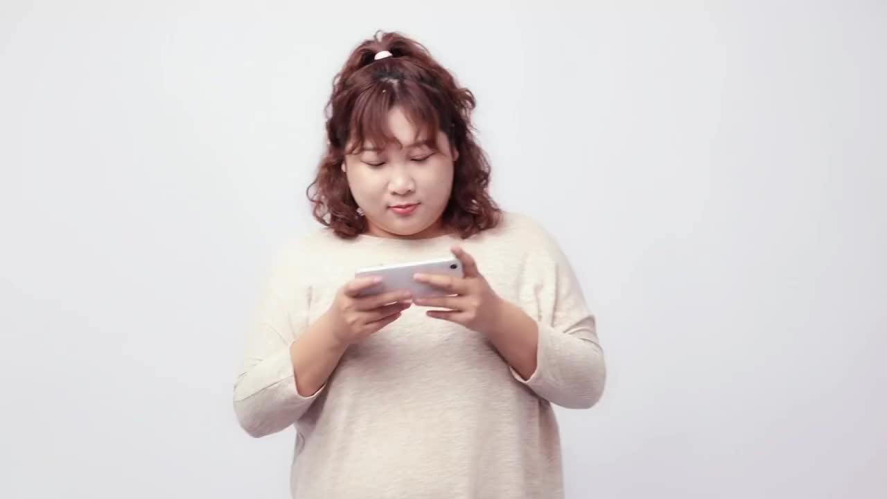 纯色背景里用手机打游戏的胖女孩视频素材