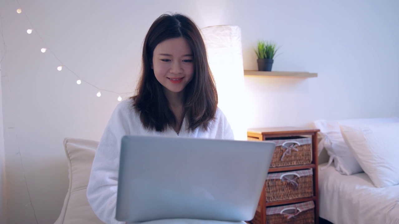 年轻女士坐在卧室用笔记本电脑视频素材