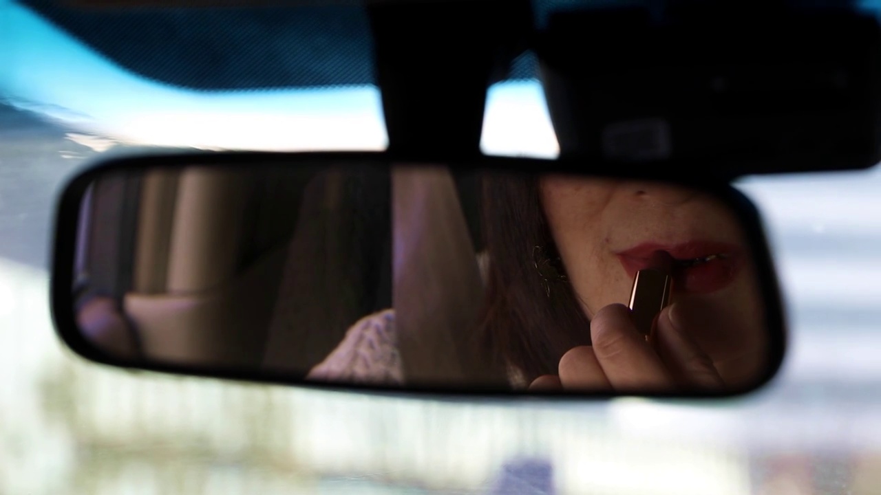 一个女人坐在汽车内对着后视镜涂口红视频素材