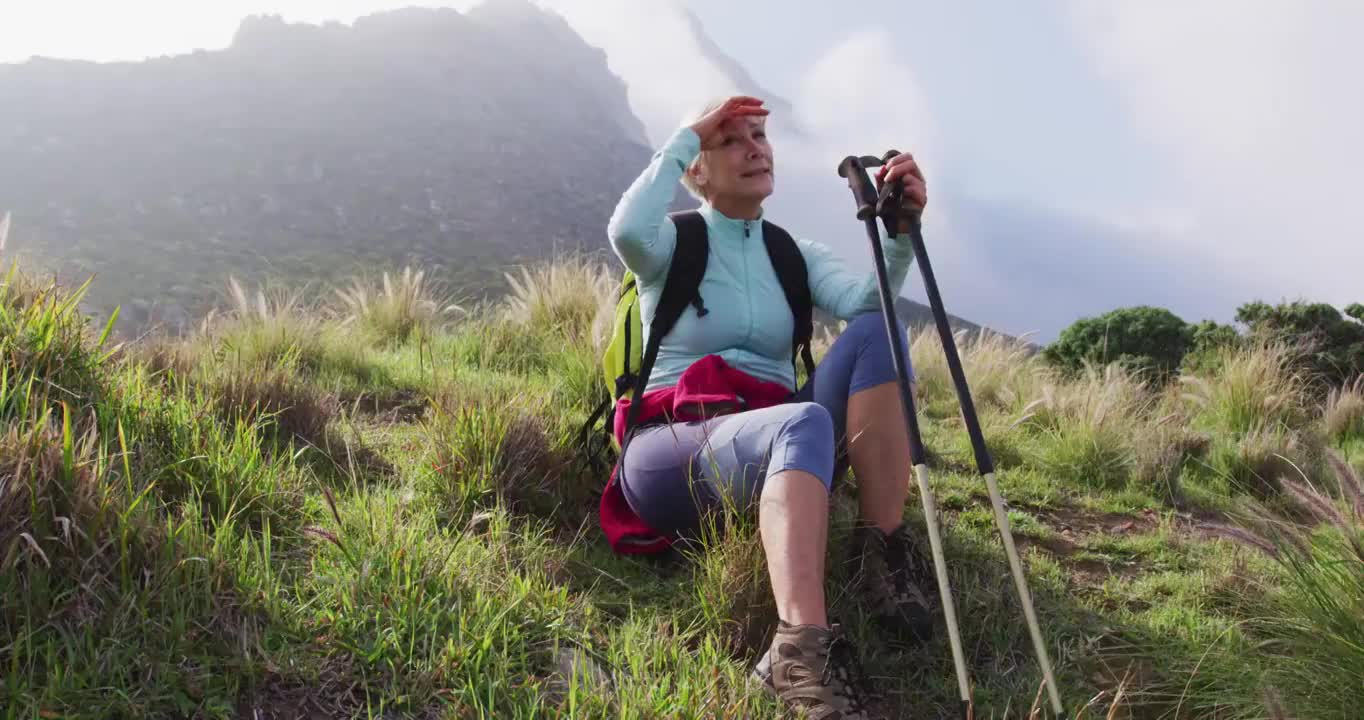 疲惫的高级徒步女坐在草地上，而徒步在山上。徒步旅行视频下载