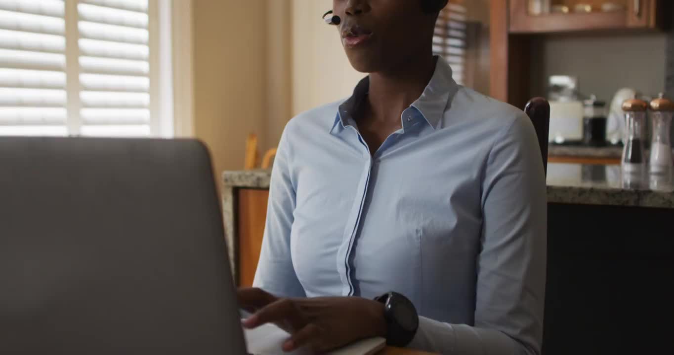 一位非裔美国妇女，在家里工作时戴着电话耳机在笔记本电脑上进行视频通话视频素材