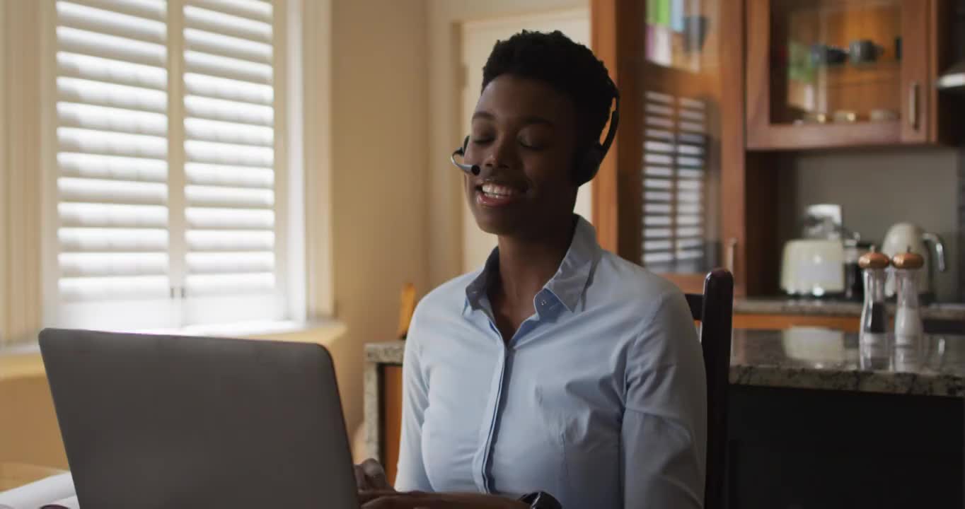一位非裔美国妇女，在家里工作时戴着电话耳机在笔记本电脑上进行视频通话视频素材