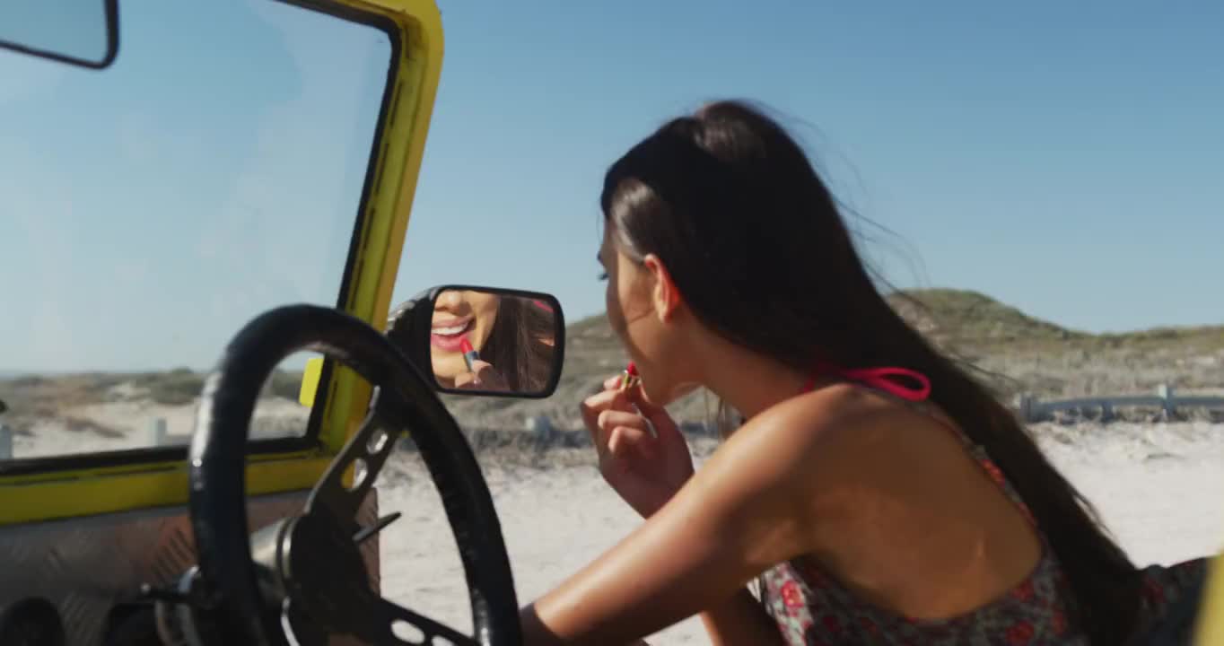 快乐的白人女人坐在沙滩车在海边做化妆视频素材