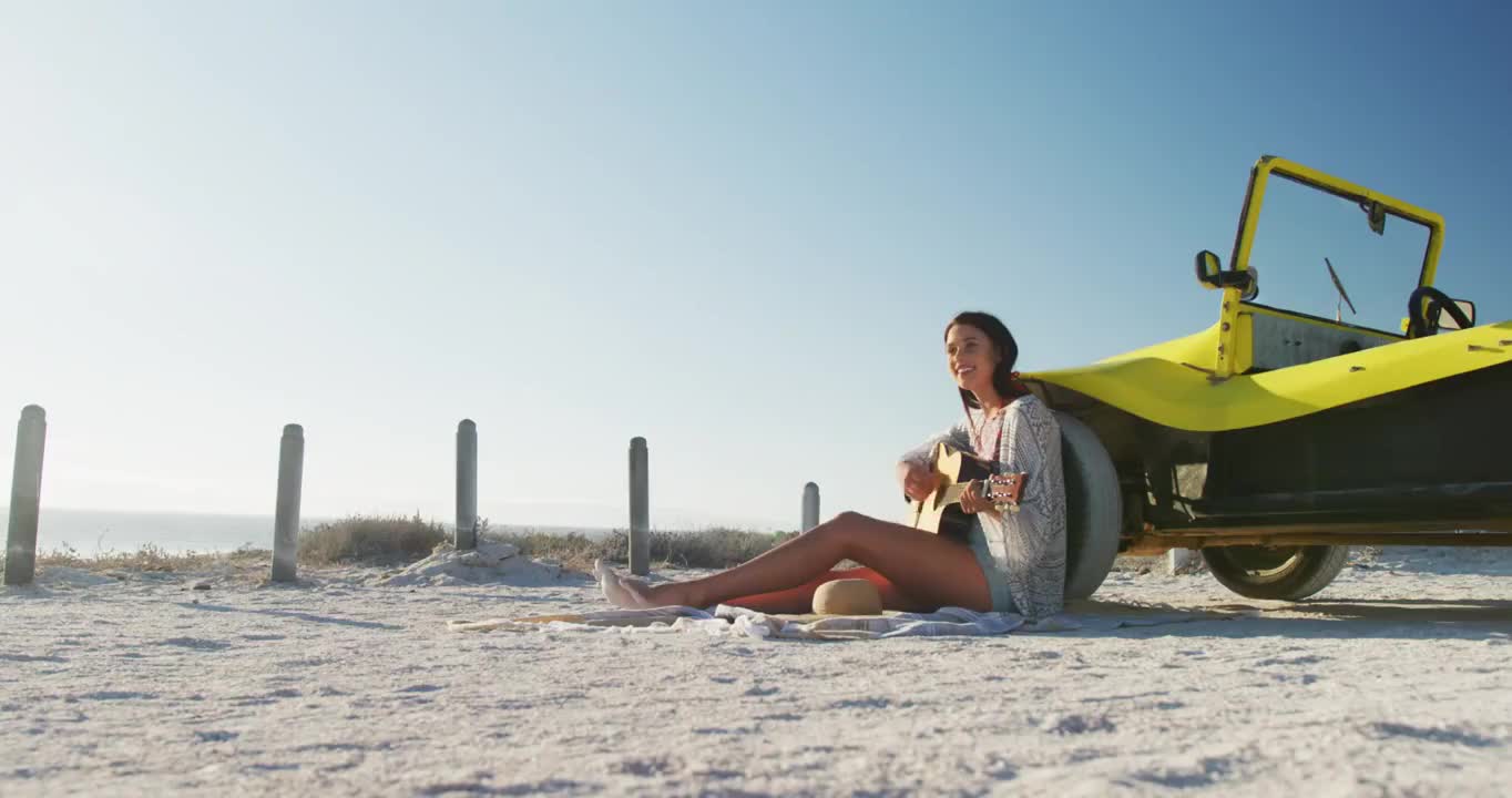 快乐的白人妇女坐在海边的沙滩车玩吉他视频素材
