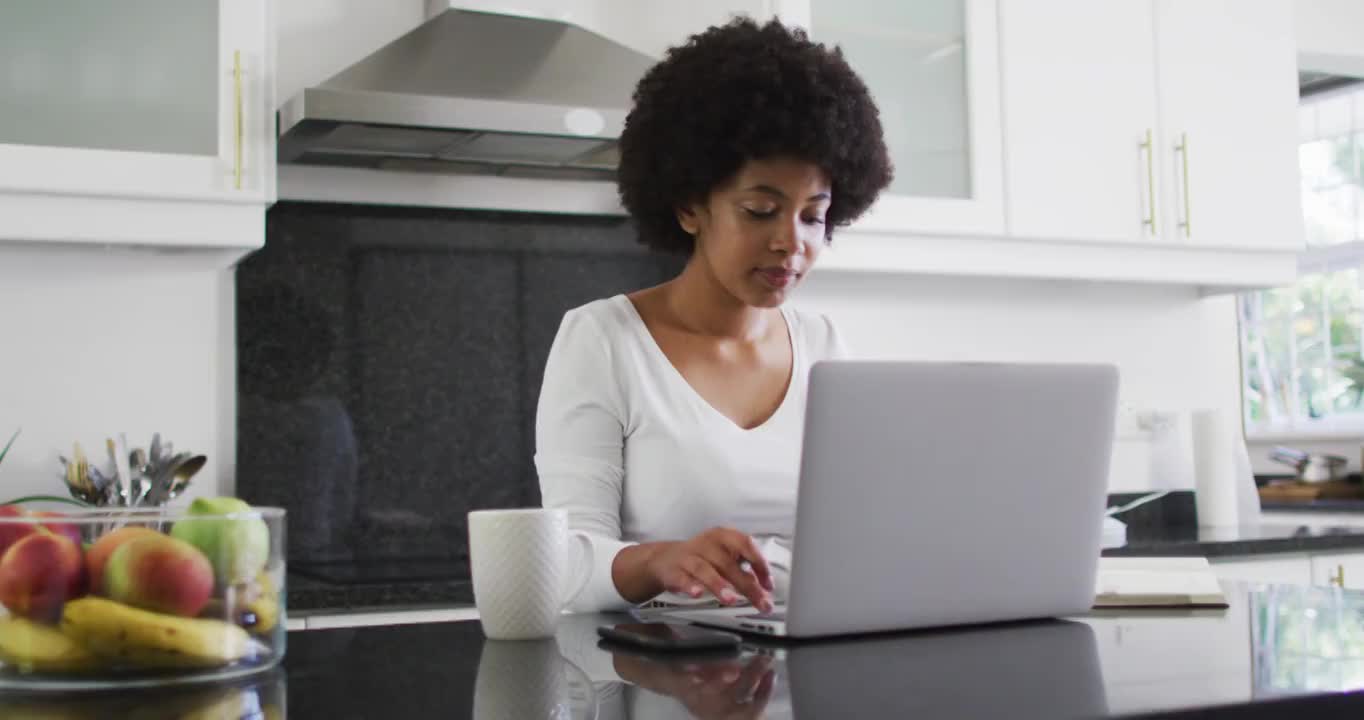 一位非裔美国妇女在家工作时在厨房使用笔记本电脑视频素材