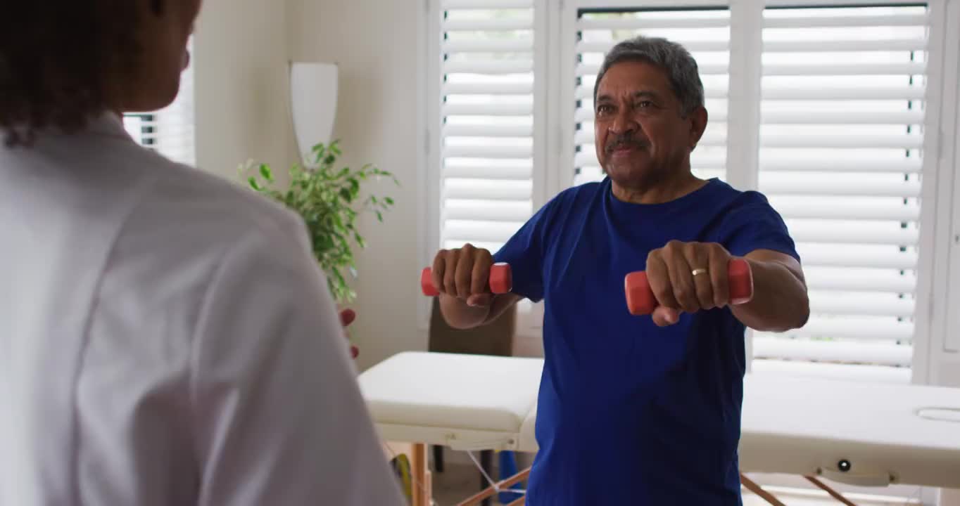 混血女性物理治疗师帮助老年男子使用哑铃锻炼视频素材