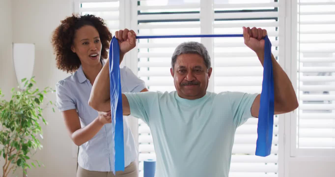 混合种族的女性物理治疗师帮助高级男子使用锻炼带锻炼视频素材
