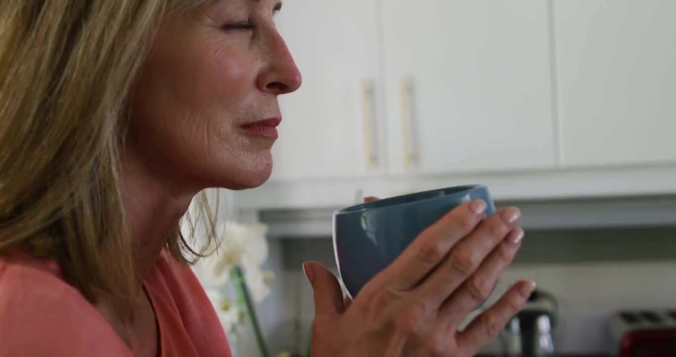 一个白人妇女站在家里的厨房里喝着咖啡视频素材