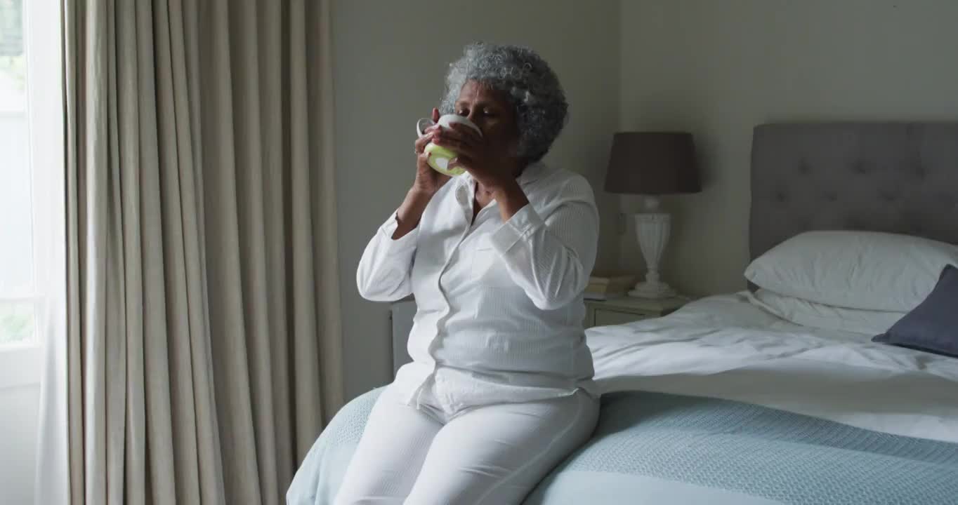 资深非洲裔美国妇女坐在家里的床上喝咖啡视频素材