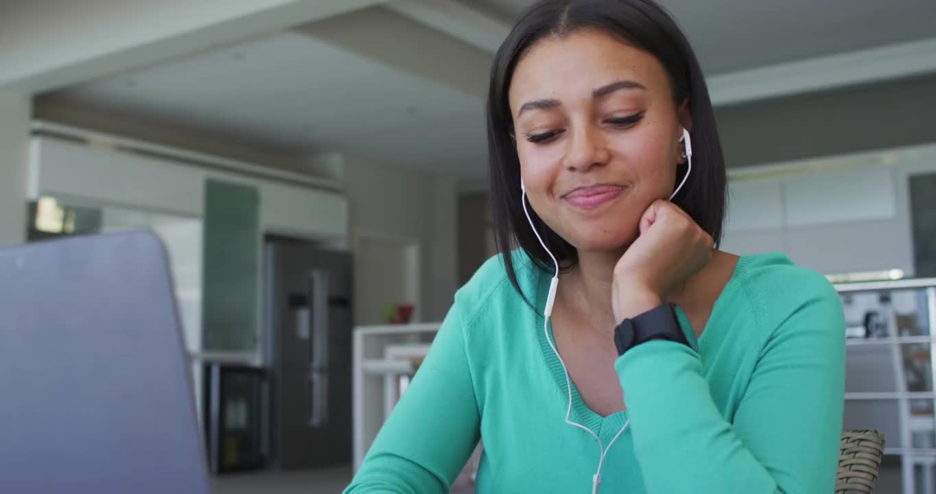 非裔美国妇女，在家工作时戴着耳机使用笔记本电脑视频素材