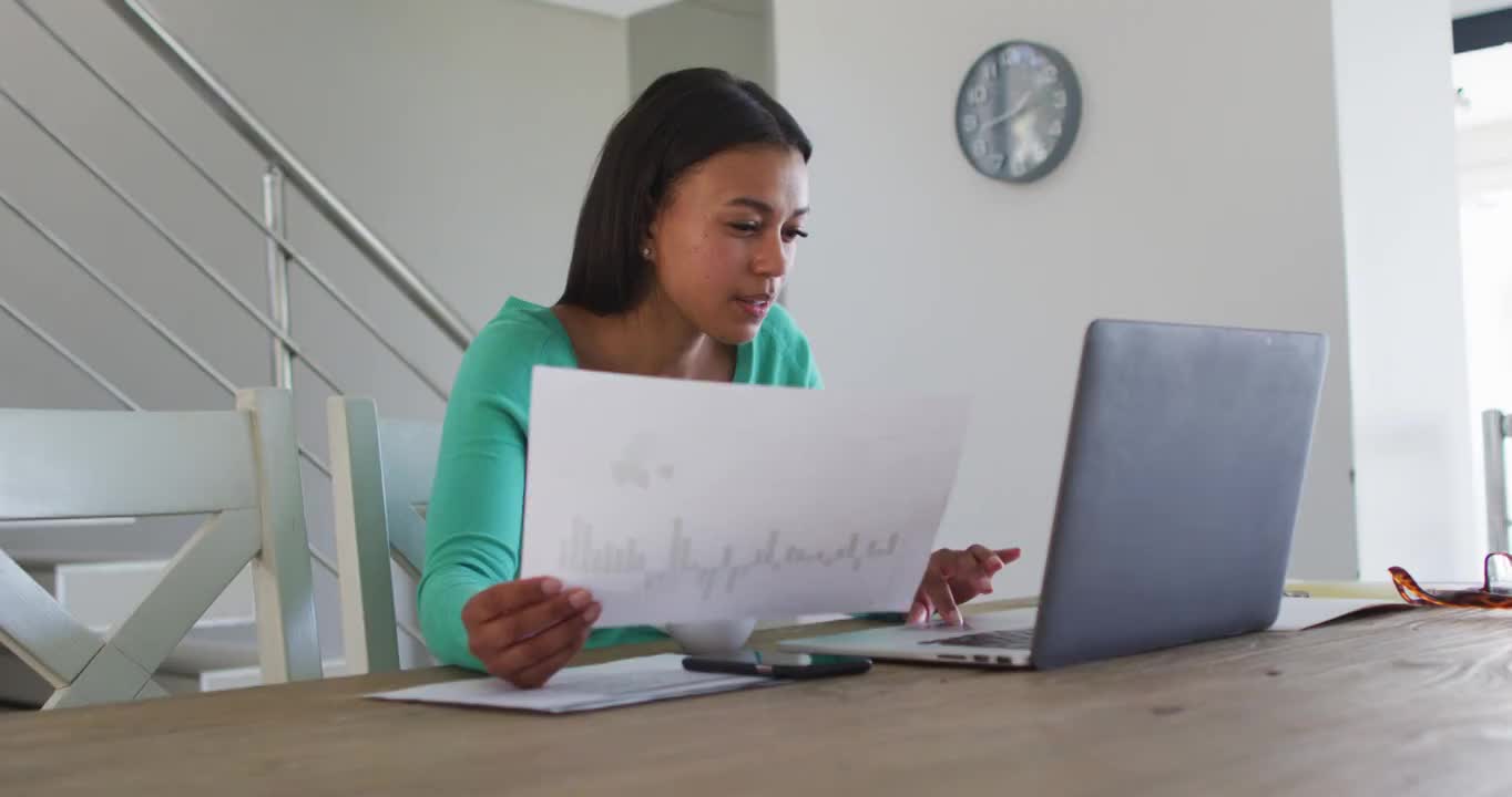 一位非裔美国妇女在家工作时阅读文件并使用笔记本电脑视频素材