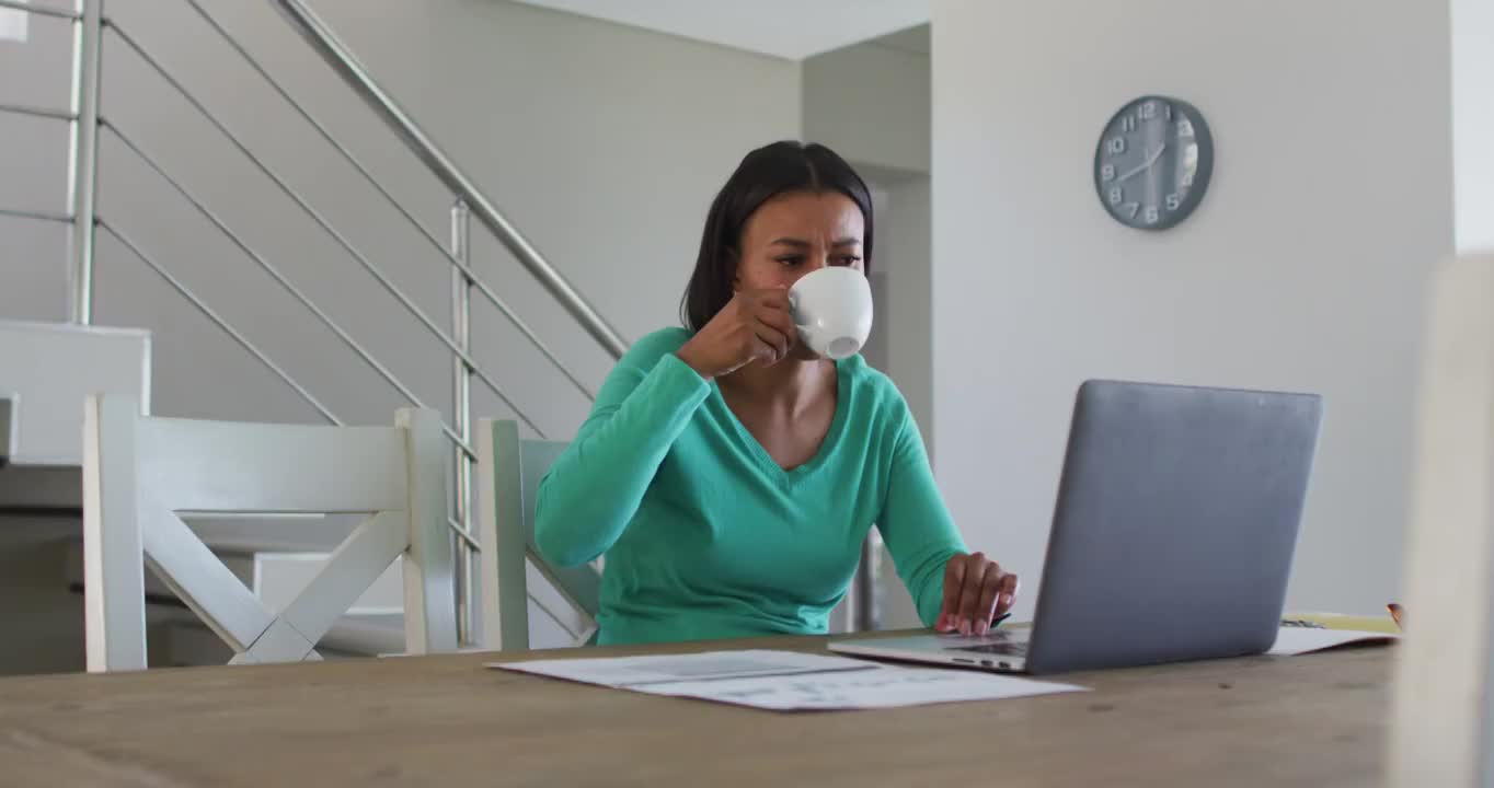 一位非裔美国妇女，在家工作时喝咖啡，用笔记本电脑视频素材