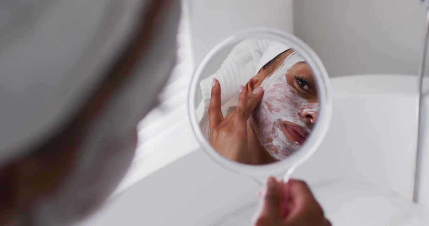 非裔美国妇女在家里浴室里拿着镜子敷面膜视频素材
