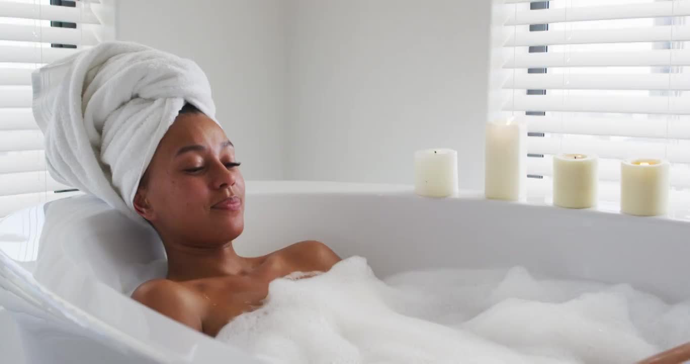 一个非裔美国妇女，在家里浴室的浴缸里吹肥皂泡视频素材