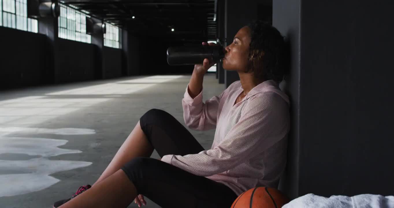 一个非裔美国女人坐在空房子里喝着水视频素材